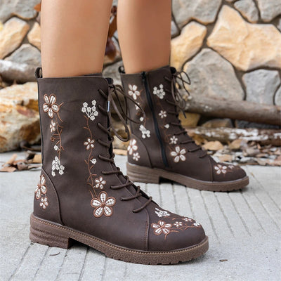 Brown boots with floral embroidery worn by a person against a stone wall background