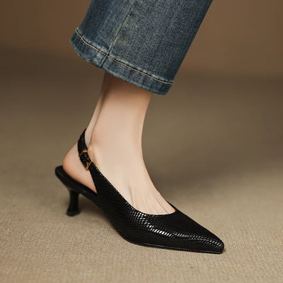 Black high-heeled shoes worn with rolled-up jeans on a neutral background