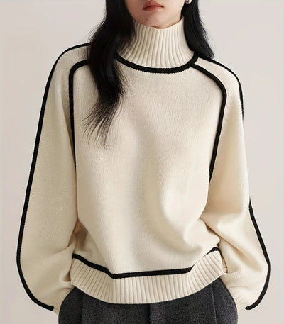 Person wearing a cream sweater with black trim on a plain background