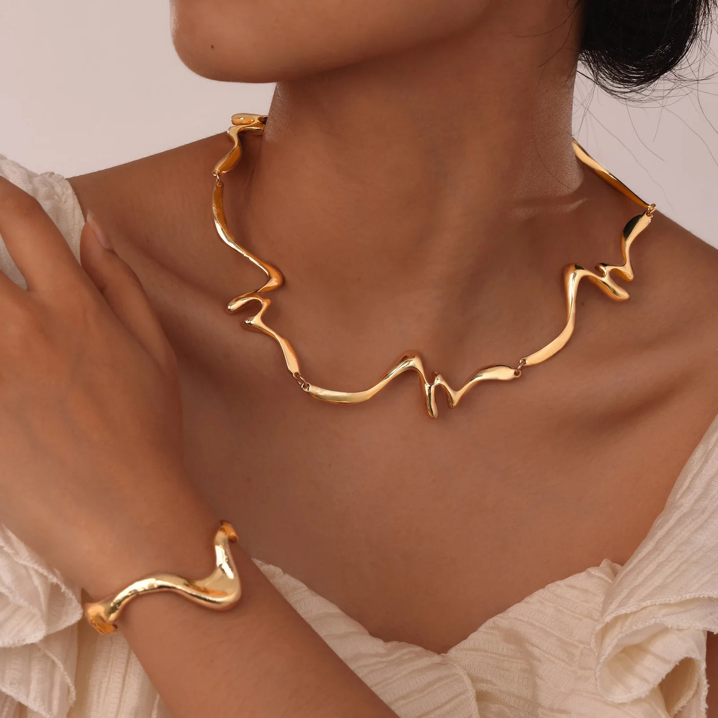 Gold necklace and bracelet on a person against a neutral background