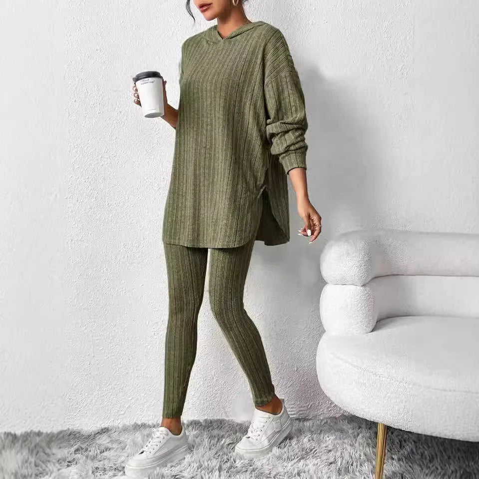Person wearing a green knit outfit holding a white cup against a white wall.