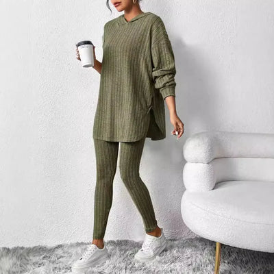 Person wearing a green knit outfit holding a white cup against a white wall.