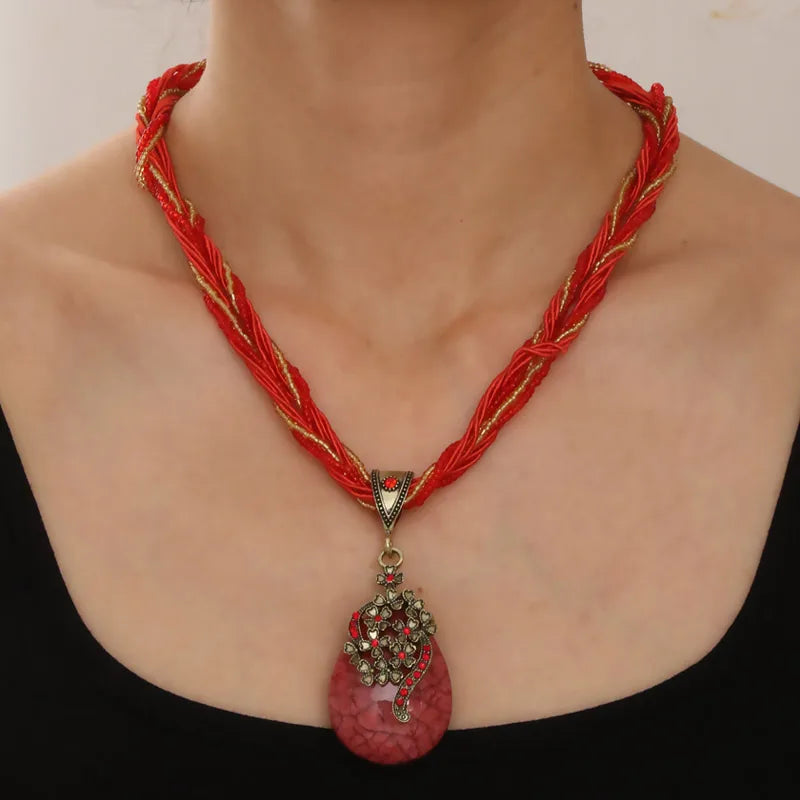 Red and gold braided necklace with a pink pendant on a person wearing a black top.