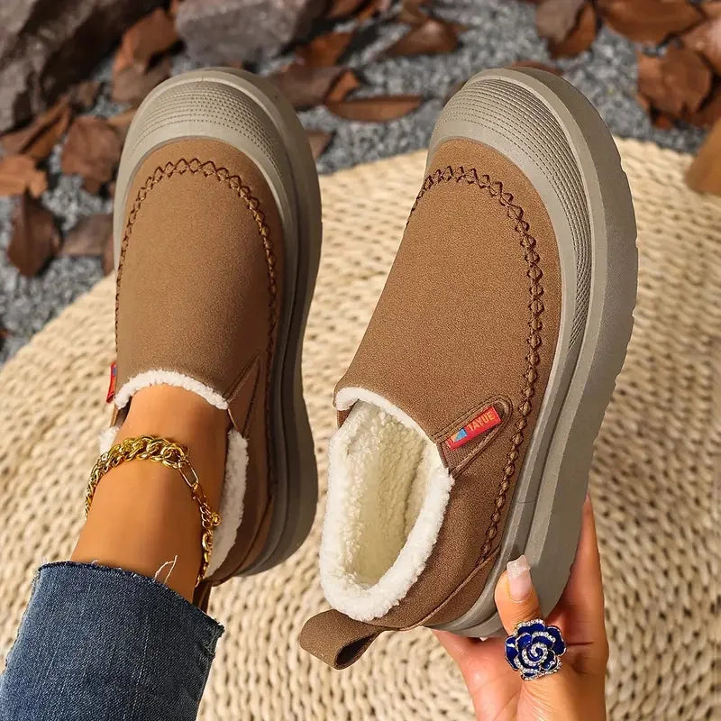 Brown winter boots with white fur lining held by a person on a textured surface.