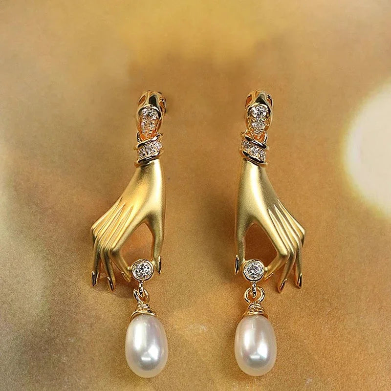 Gold hand-shaped earrings with pearl drops on a gold background