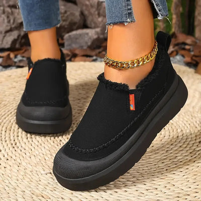 Black slip-on shoes worn with denim jeans on a woven surface.