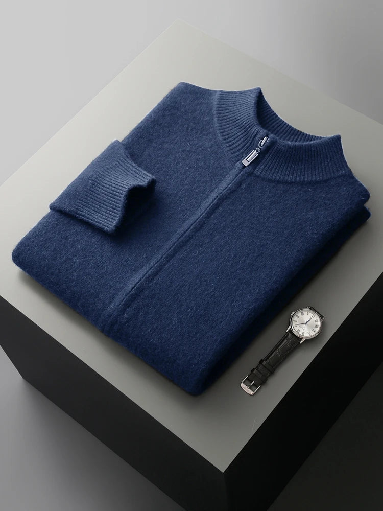 Folded blue sweater on a light gray surface with a black watch beside it.