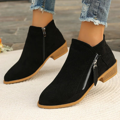 Black ankle boots with brown soles worn with denim jeans on a neutral background