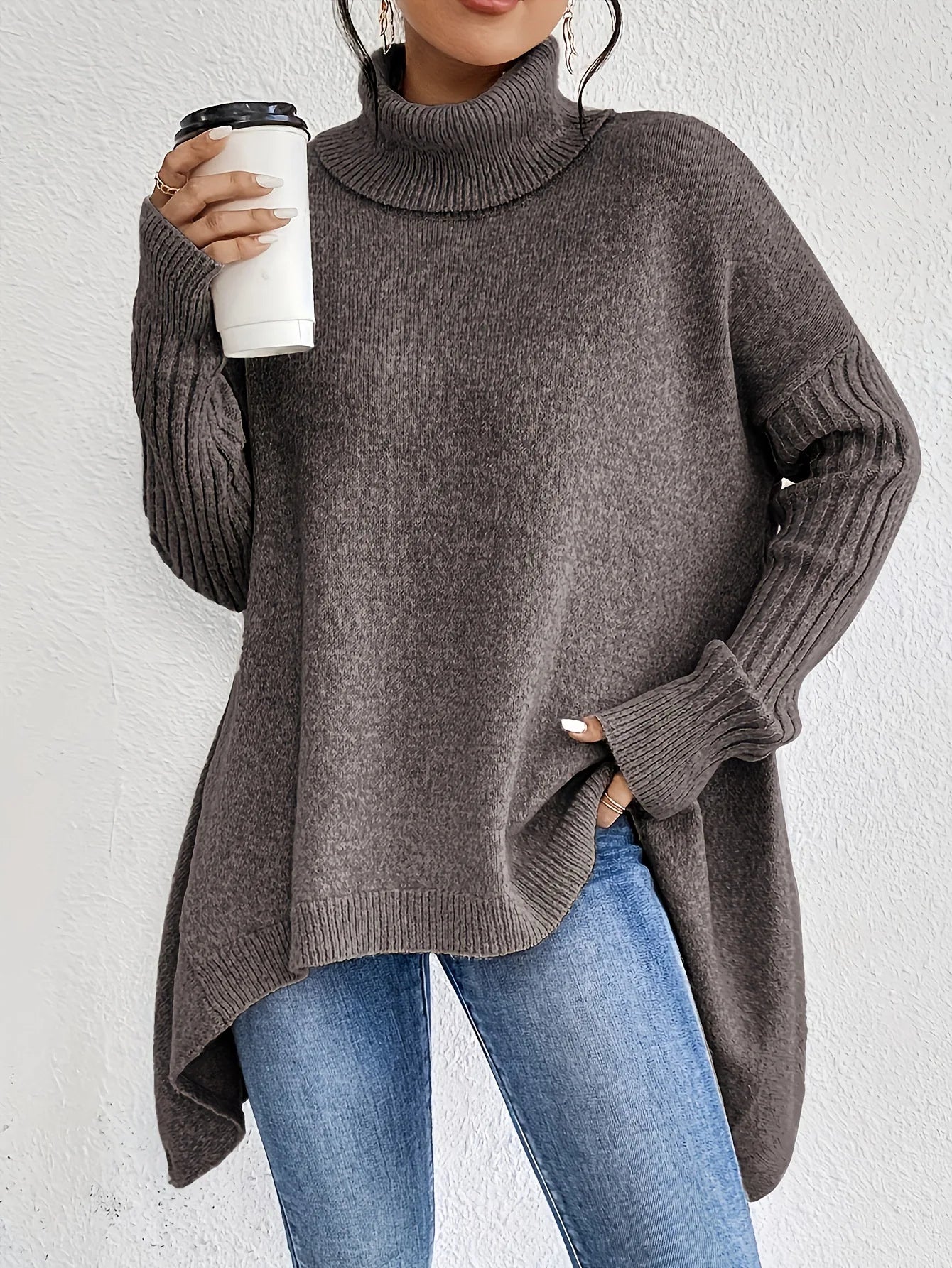 Person wearing a gray sweater and blue jeans holding a white cup against a light background