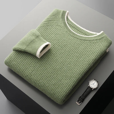 Folded green sweater on a gray surface with a watch beside it