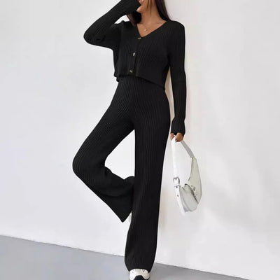 Person wearing a black ribbed jumpsuit holding a white bag against a white background