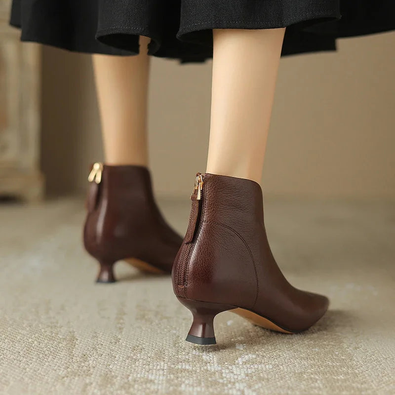 Brown ankle boots with gold zippers worn by a person on a neutral background