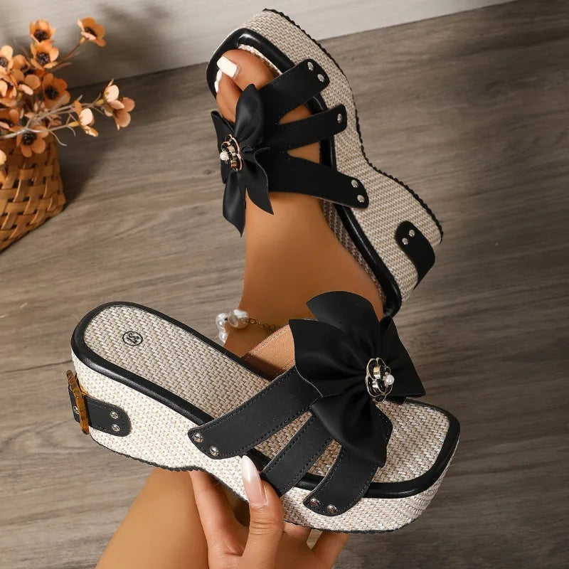 Black and white sandals with bow details on a wooden floor.