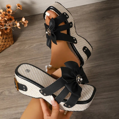 Black and white sandals with bow details on a wooden floor.