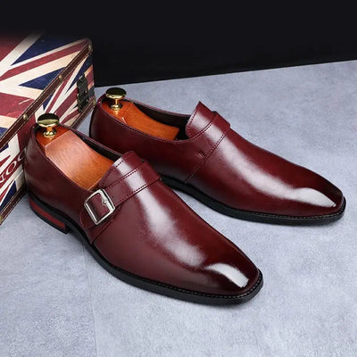 Pair of brown leather shoes with a buckle on a gray surface, Union Jack flag in the background.