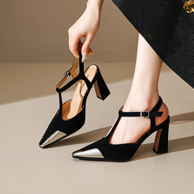 Black high-heeled shoes with metallic accents worn by a person on a beige background
