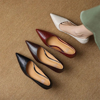 Set of four pointed-toe shoes in black, brown, red, and white on a beige surface.