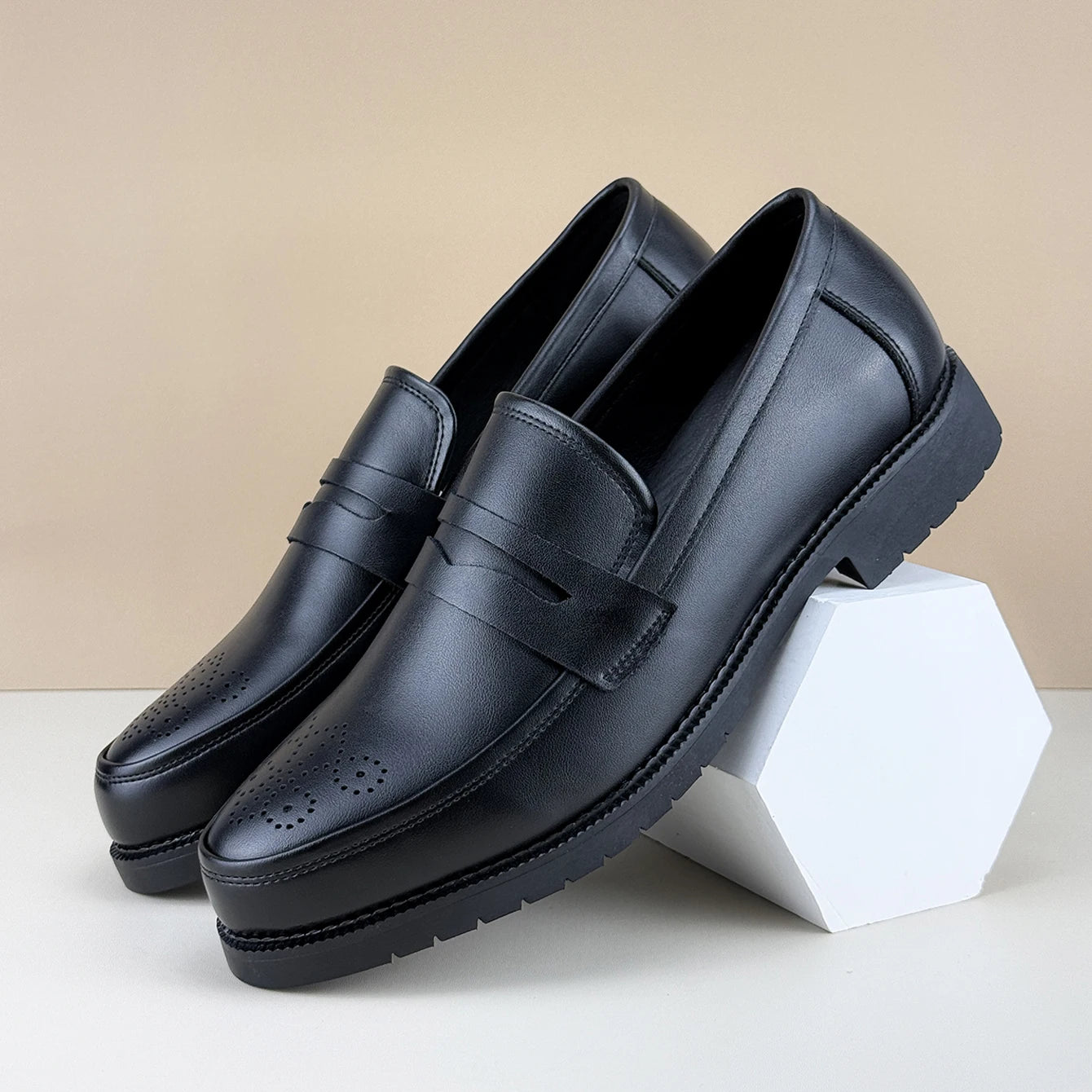Pair of black leather loafers on a white surface with a beige background