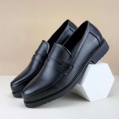 Pair of black leather loafers on a white surface with a beige background