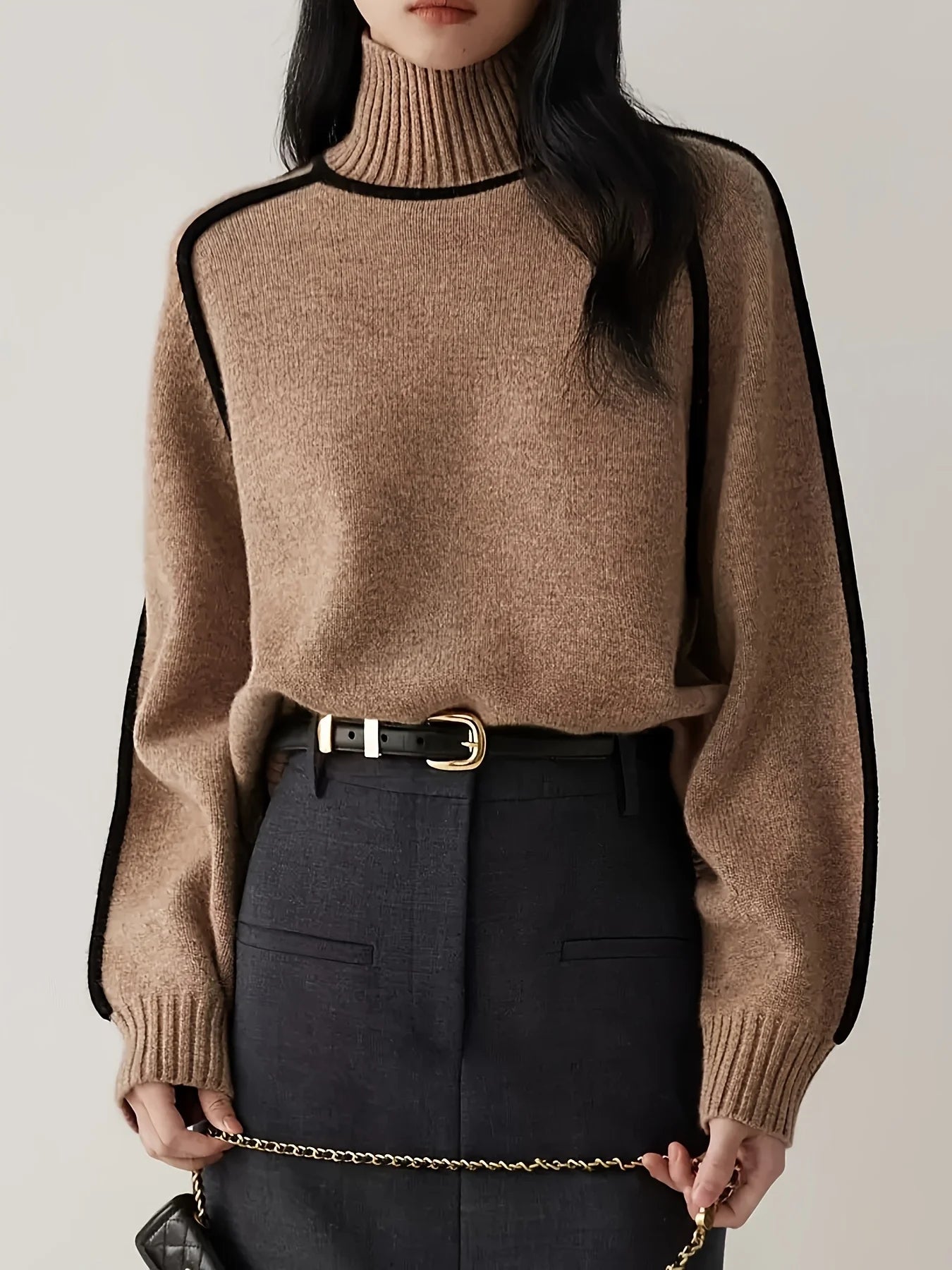 Person wearing a brown turtleneck sweater with black accents and black pants.
