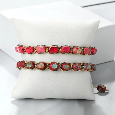 Two bracelets with pink and green gemstones on a white cushion