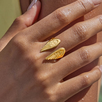 Gold wing-shaped earrings on a hand with a blurred background