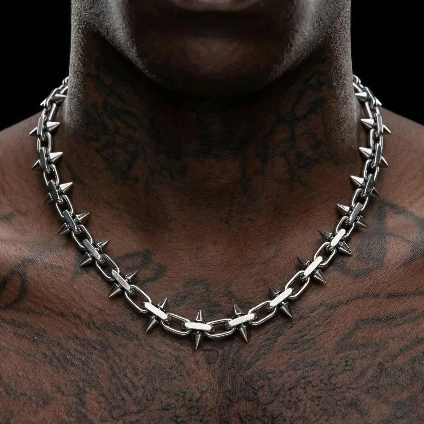 Necklace with spikes worn by a person with tattoos on a black background