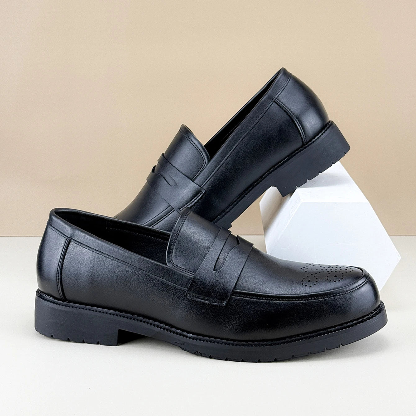 Black leather loafers on a beige and white background