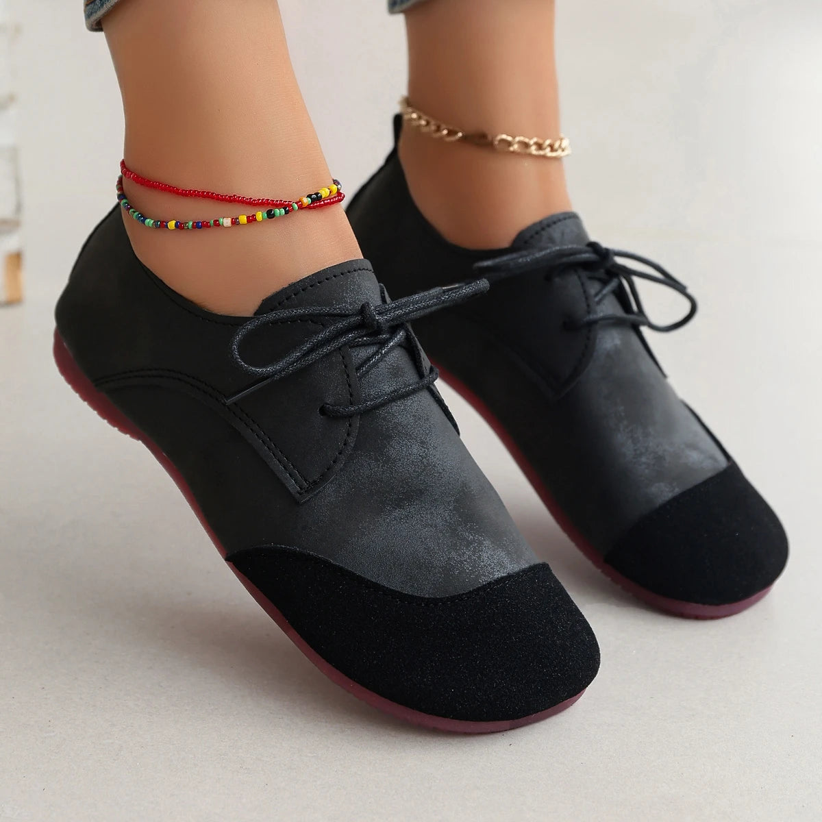 Black shoes with red soles worn by a person on a light gray background