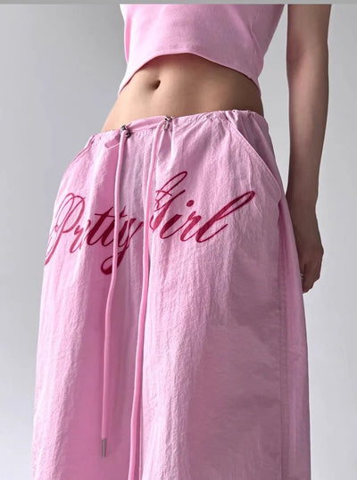 Pink skirt with 'Bitty Girl' text worn by a person on a plain background