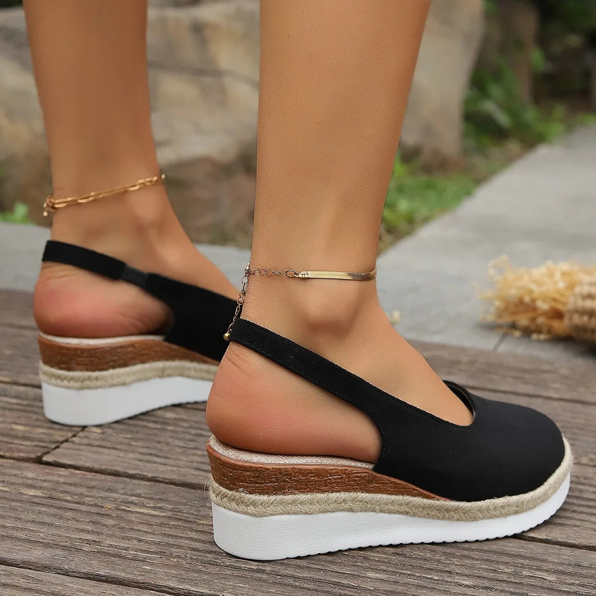 Black wedge sandals with wooden sole worn on a wooden floor.