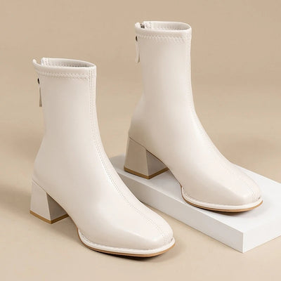 White ankle boots with block heels on a beige background