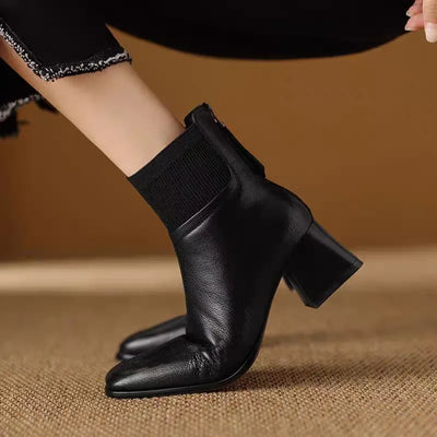 Black leather ankle boots with block heels on a brown textured surface