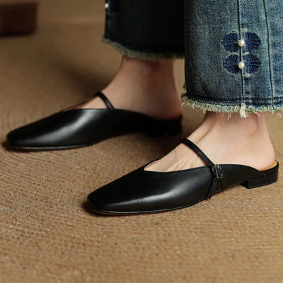 Black flat shoes worn with denim jeans on a brown surface