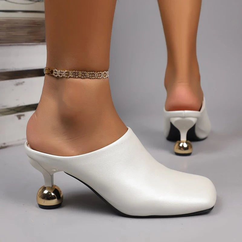 White high-heeled shoes with gold accents worn by a person on a neutral background