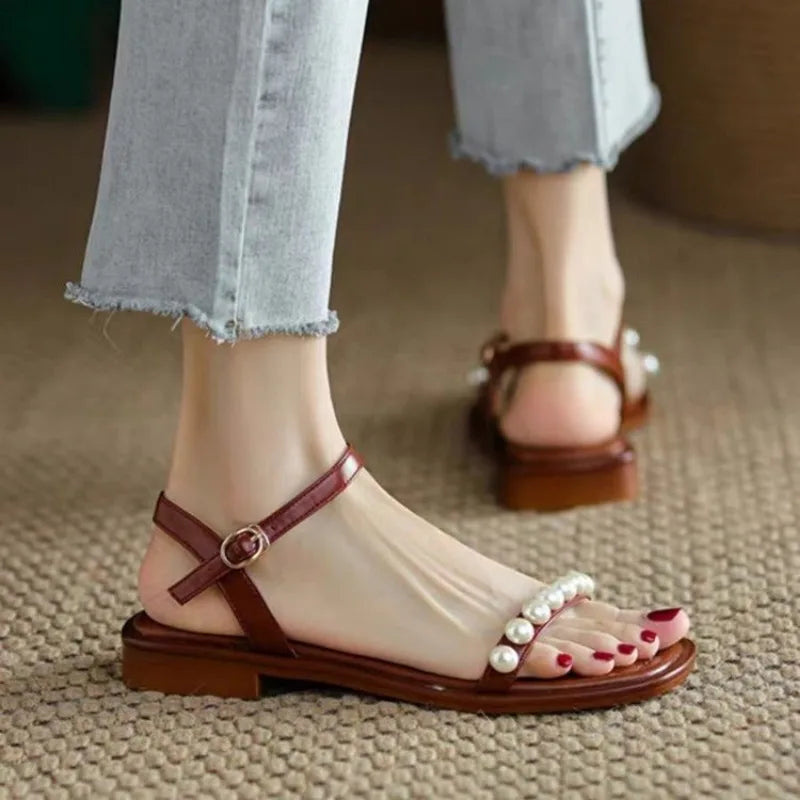 Brown sandals with pearl details worn with light blue jeans on a textured surface.
