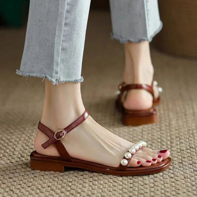 Brown sandals with pearl details worn with light blue jeans on a textured surface.