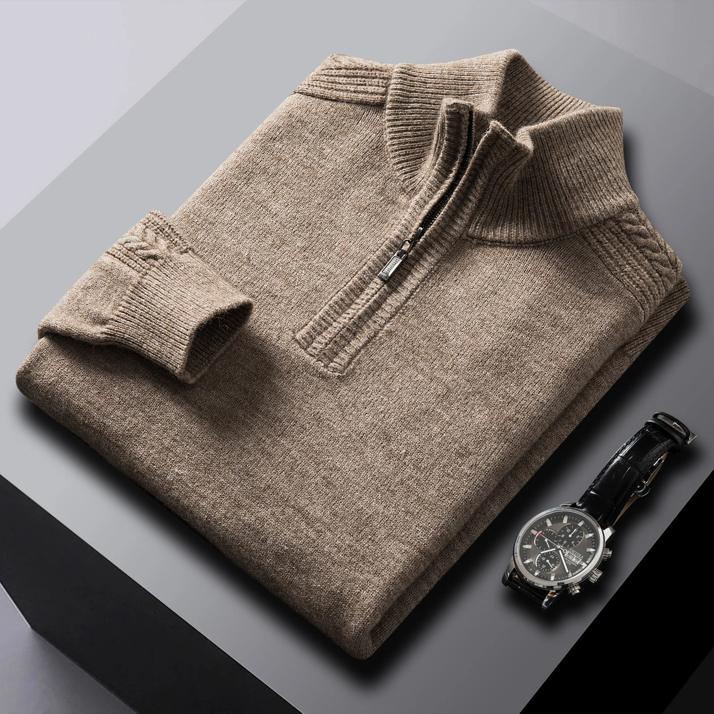 Folded brown sweater on a gray surface with a black watch beside it