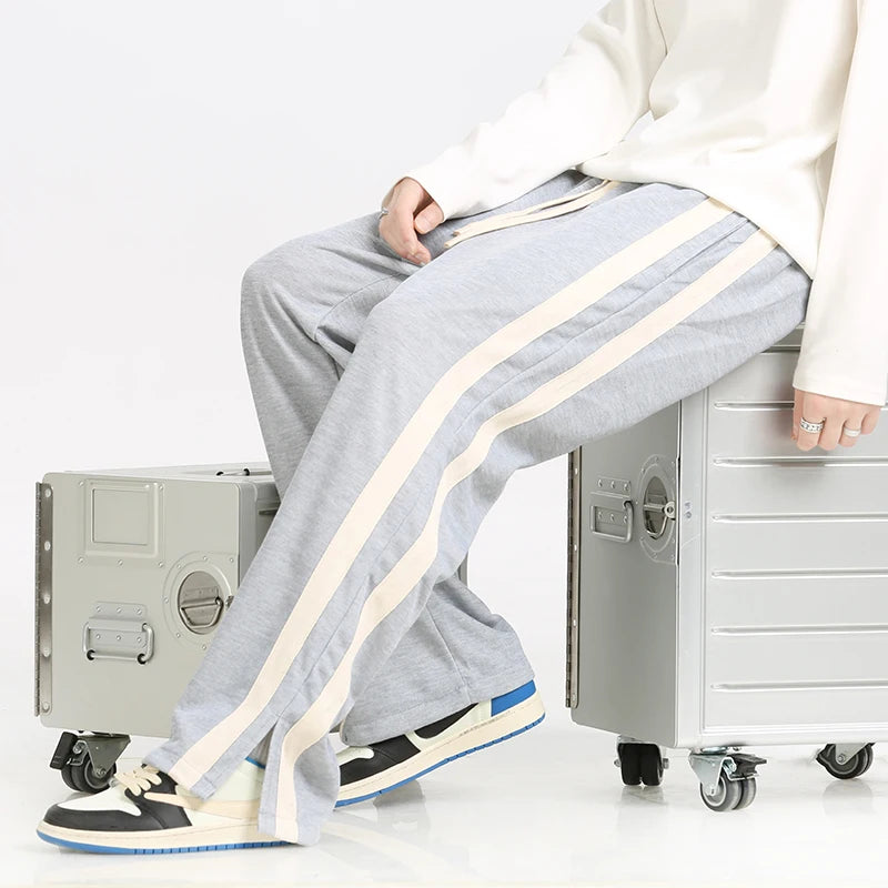 Person wearing gray sweatpants with white stripes sitting on a metal box against a white background