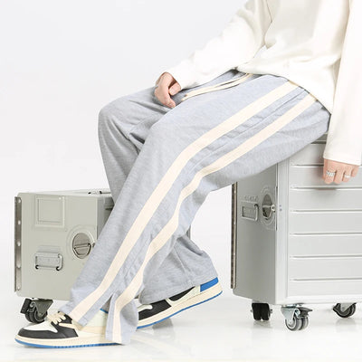 Person wearing gray sweatpants with white stripes sitting on a metal box against a white background