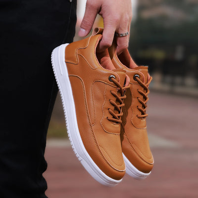 Brown sneakers with white soles held by a person outdoors