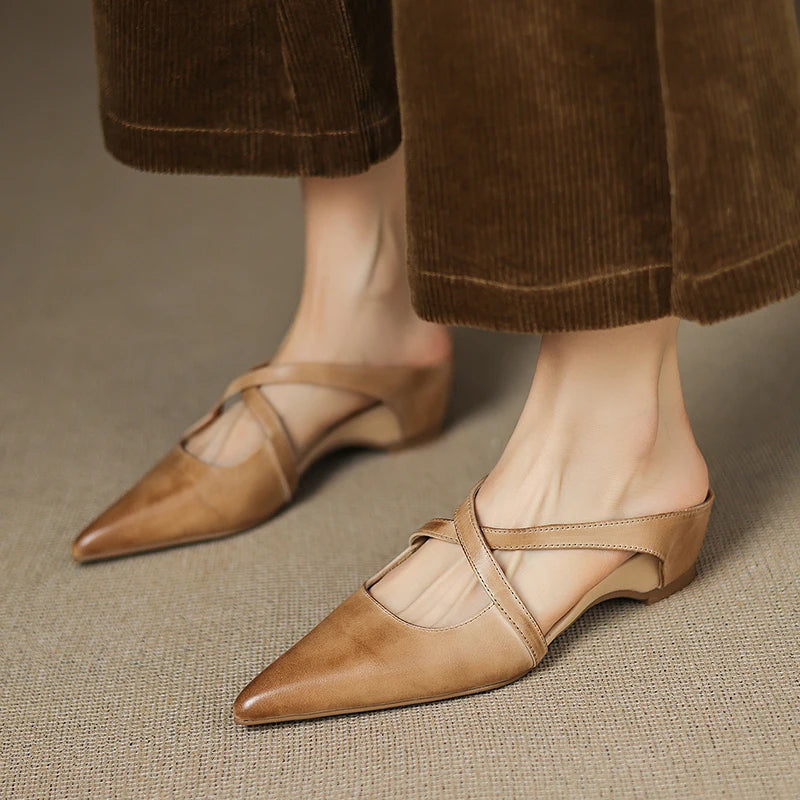 Brown pointed-toe shoes worn with brown pants on a neutral background
