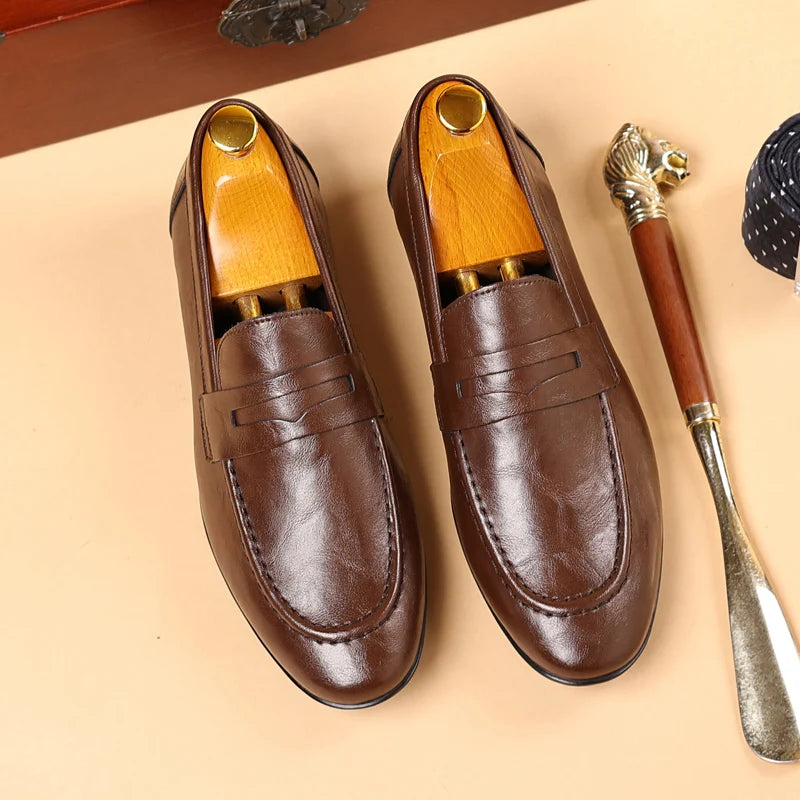 Pair of brown leather loafers with wooden soles on a beige surface.