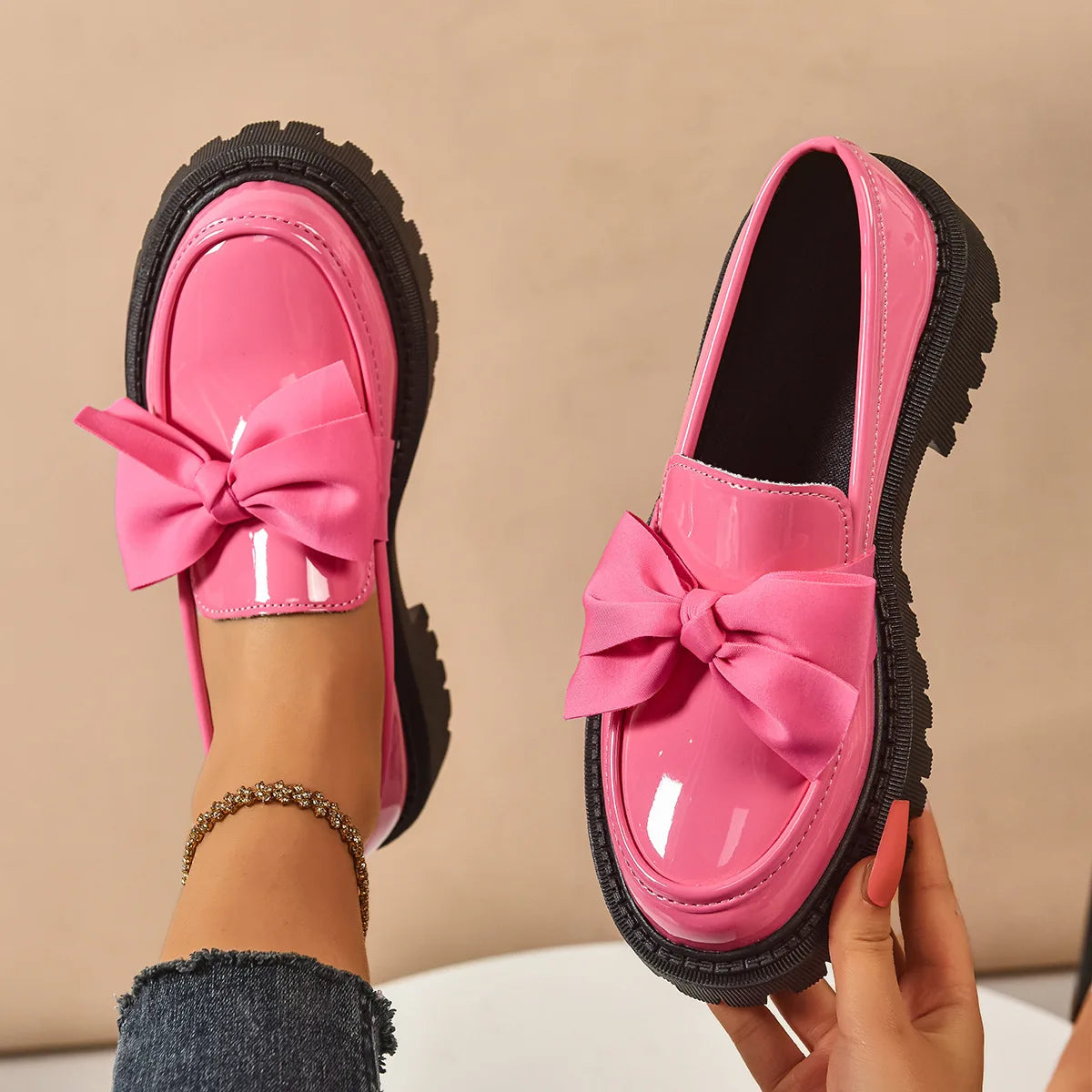 Pink loafers with a bow held by a person against a beige background