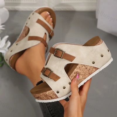 Beige sandals with brown straps held by a hand on a neutral background