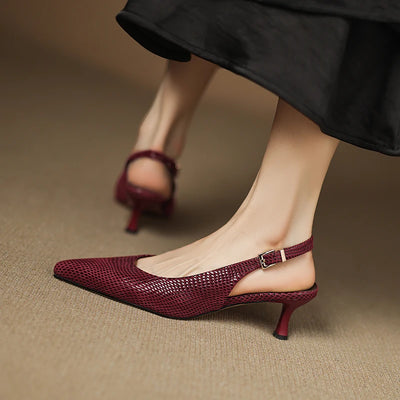 Maroon high-heeled shoes worn with a black skirt on a brown background