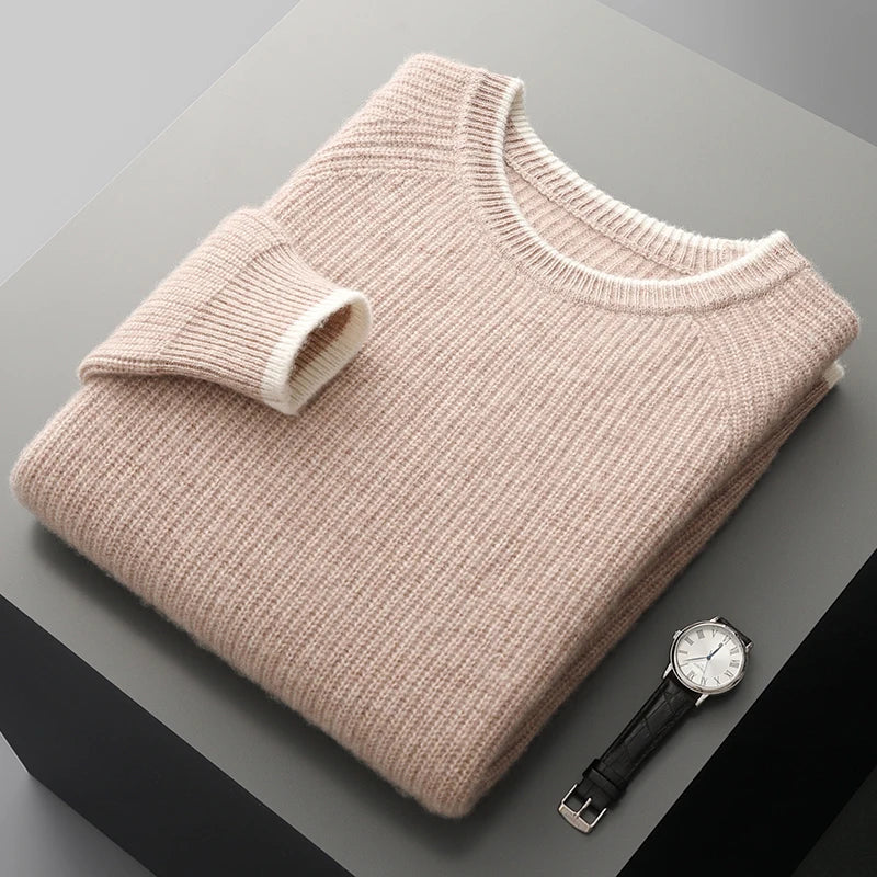 Folded beige sweater on a gray surface with a watch beside it