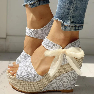 White lace wedge sandals with a bow worn with denim jeans.
