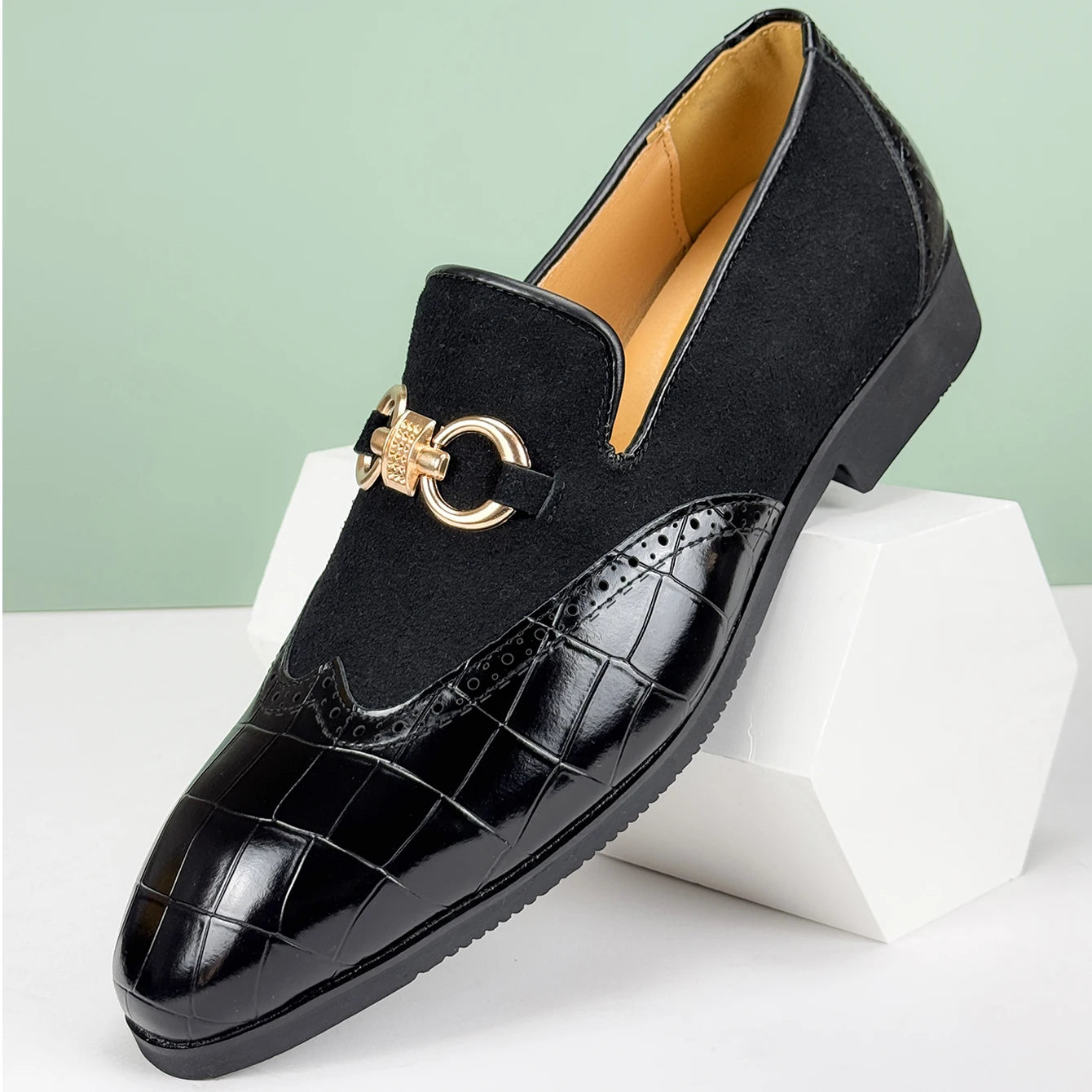Black loafers with gold accents on a white stand against a light green background
