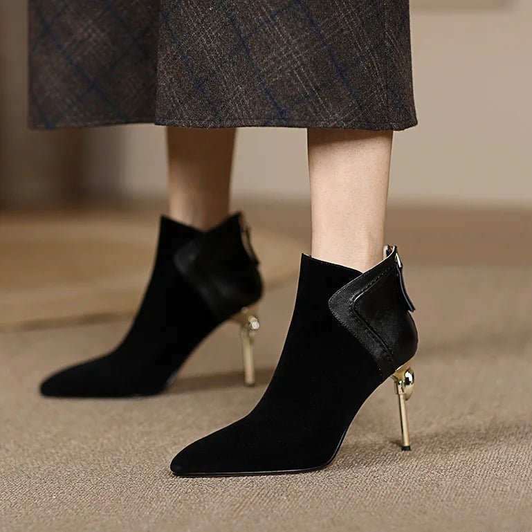 Black ankle boots with gold heels worn by a person on a beige carpet.